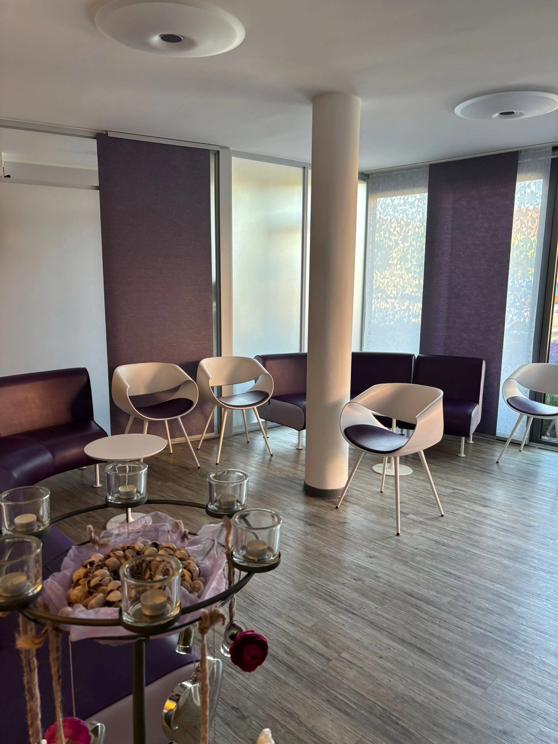 Frauenarztpraxis Dr. A. Dietrich - Gesundheitsdienste für Frauen - Ein Wartezimmer mit lila Sofas, weißen modernen Stühlen und einem runden Mitteltisch.