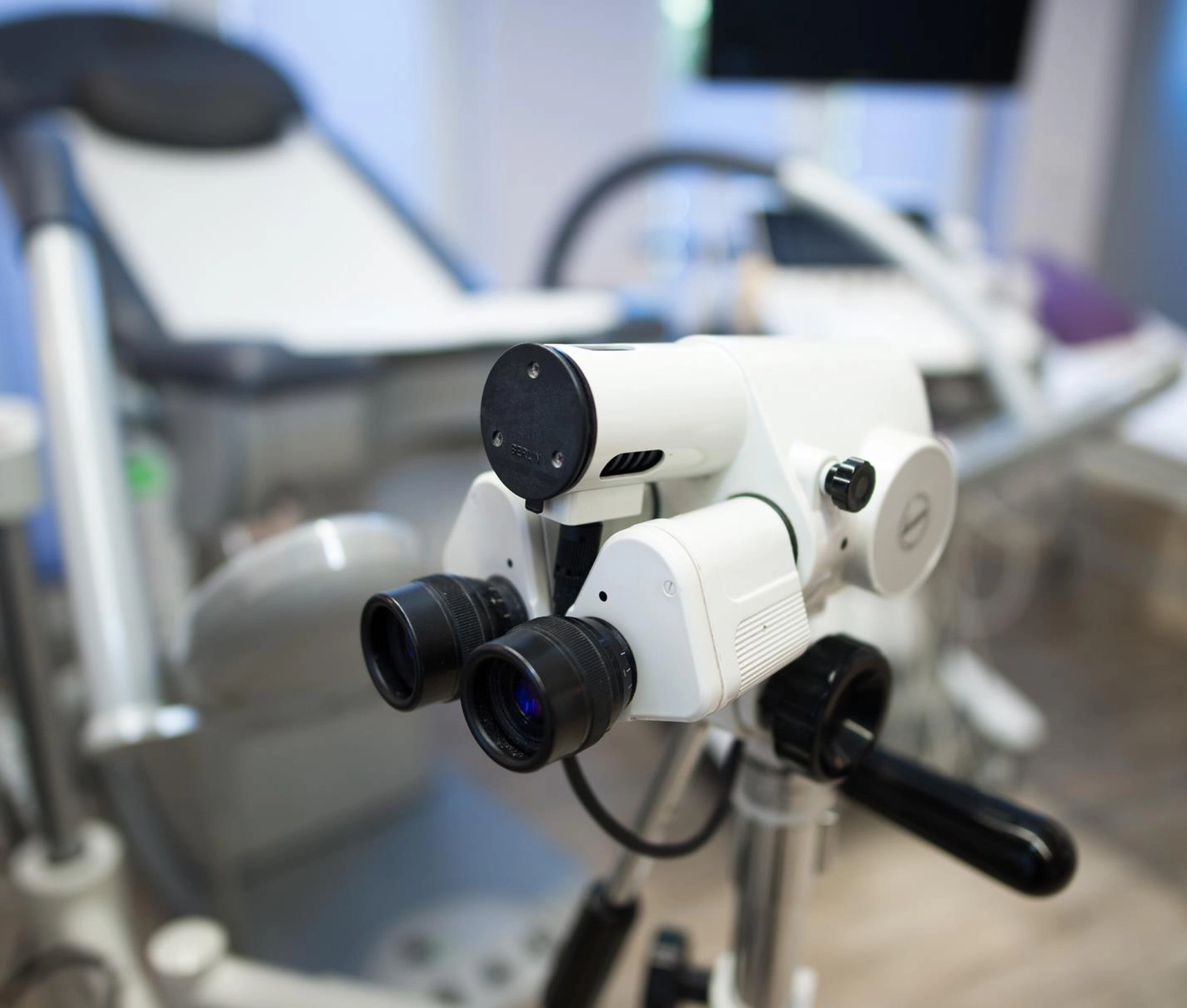 Frauenarztpraxis Dr. A. Dietrich - Gesundheitsdienste für Frauen - Ein hochmodernes medizinisches Kolposkop mit zwei Okularen im Vordergrund eines modernen Untersuchungsraums.