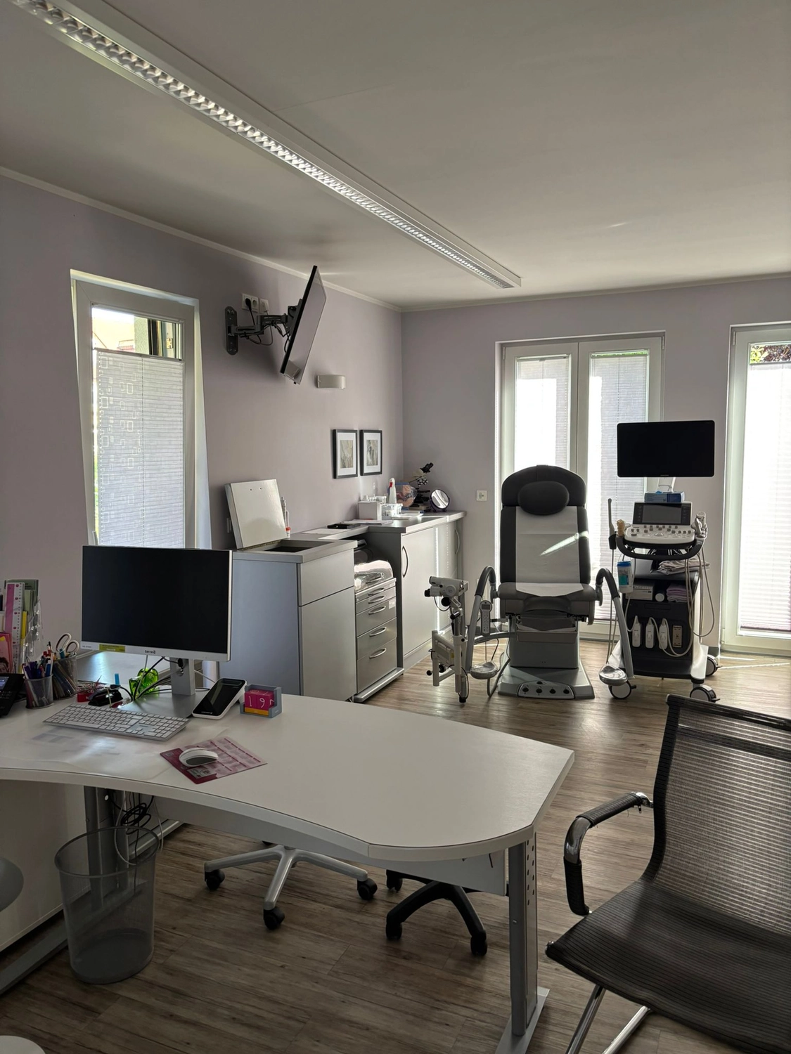 Frauenarztpraxis Dr. A. Dietrich - Gesundheitsdienste für Frauen - Ein Büro mit medizinischer Ausrüstung, darunter ein Untersuchungsstuhl und Monitore, sowie ein weißer Schreibtisch mit Computer und Bürostuhl.